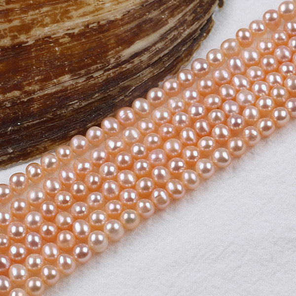 Pink freshwater pearls strands displayed on white cloth beside a natural oyster shell