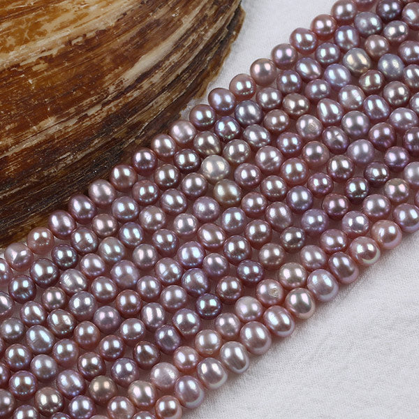Purple freshwater pearls with natural luster displayed beside a shell on a light surface